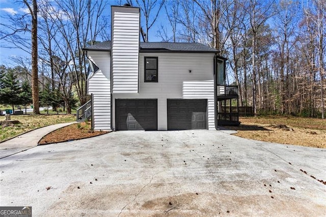 view of side of home with concrete driveway, an attached garage, and a chimney
