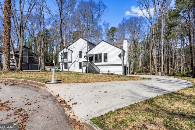 view of side of property featuring a chimney, aphalt driveway, and a lawn