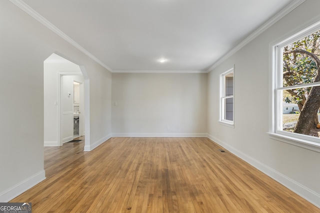 unfurnished room with arched walkways, a healthy amount of sunlight, light wood finished floors, and baseboards