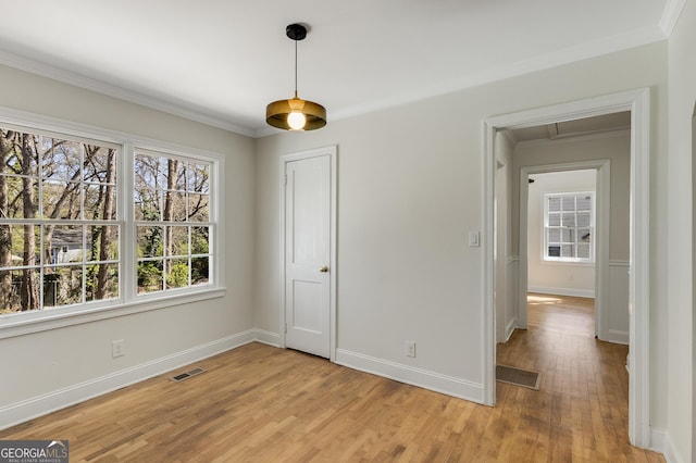 unfurnished dining area with visible vents, baseboards, ornamental molding, and light wood-style flooring