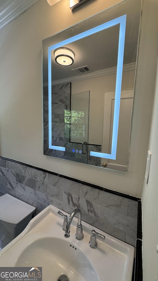 bathroom with crown molding, toilet, visible vents, tile walls, and a sink