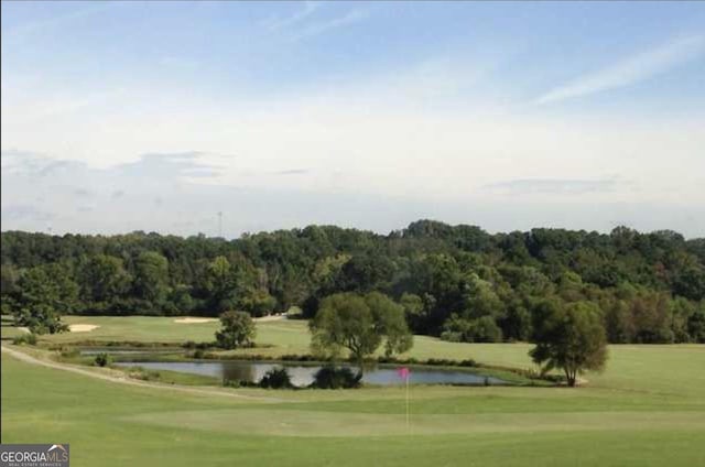 view of property's community with view of golf course, a yard, a forest view, and a water view