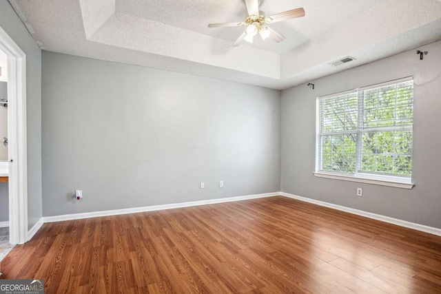 unfurnished room featuring wood finished floors, baseboards, visible vents, a tray ceiling, and a textured ceiling