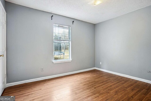 spare room featuring baseboards, a textured ceiling, and wood finished floors