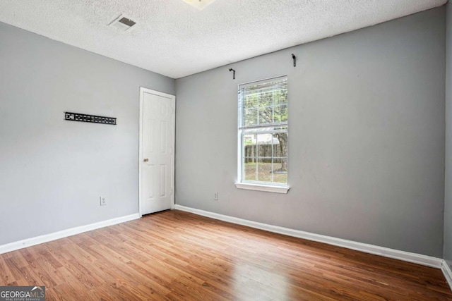 spare room featuring visible vents, wood finished floors, baseboards, and a textured ceiling