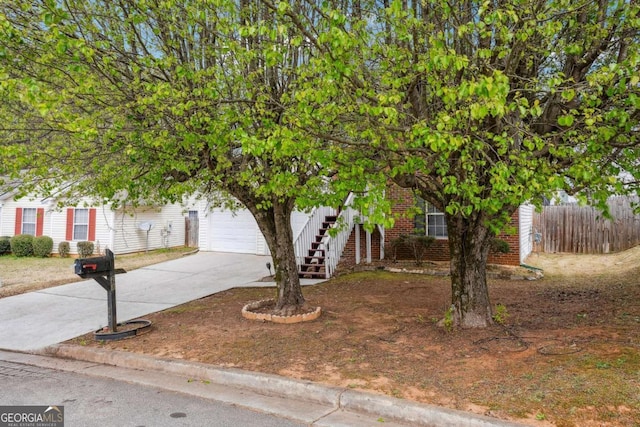 view of property hidden behind natural elements with fence, stairs, concrete driveway, a garage, and brick siding