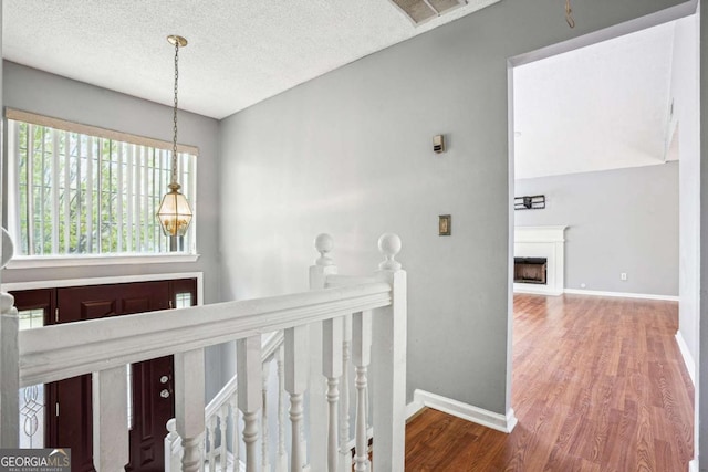 hall featuring visible vents, baseboards, an upstairs landing, wood finished floors, and a textured ceiling