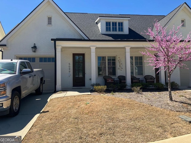 5099 Noble Village Way, Lilburn, GA 30047 - view of front facade featuring driveway, a porch, a shingled roof, a garage, and brick siding