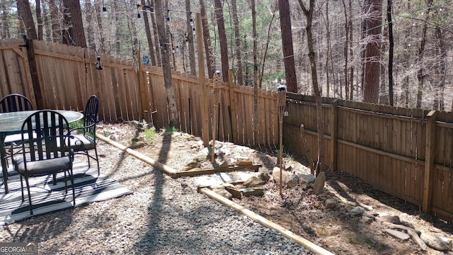 view of yard with a view of trees, outdoor dining area, and a fenced backyard