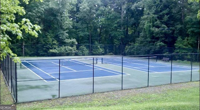 view of tennis court featuring a wooded view and fence
