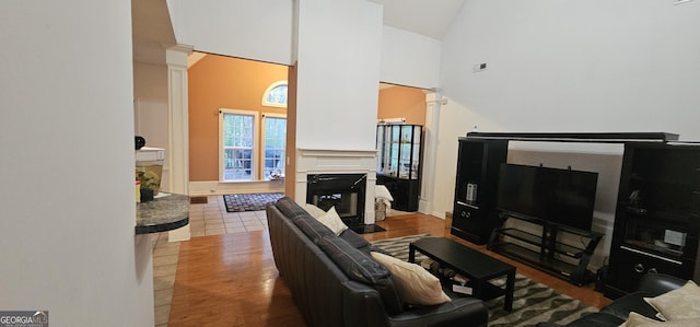 living area featuring high vaulted ceiling, decorative columns, wood finished floors, and a glass covered fireplace