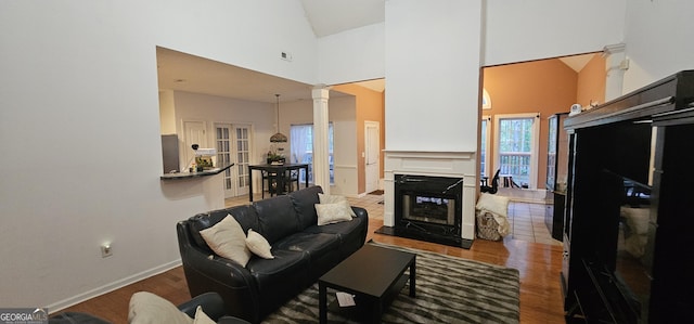 living room featuring wood finished floors, high vaulted ceiling, baseboards, and decorative columns