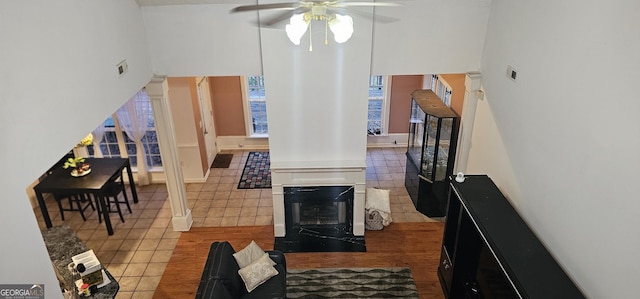 tiled living area featuring ceiling fan, decorative columns, a high ceiling, and a glass covered fireplace