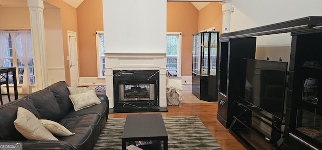 living area with decorative columns, high vaulted ceiling, a multi sided fireplace, and wood finished floors