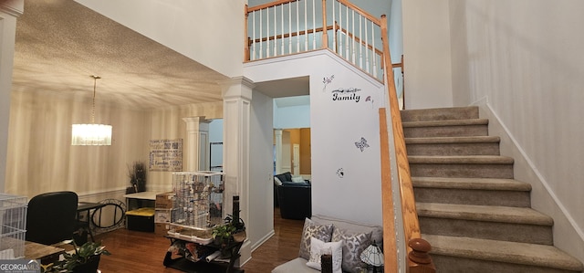 staircase with a high ceiling, decorative columns, a notable chandelier, and wood finished floors