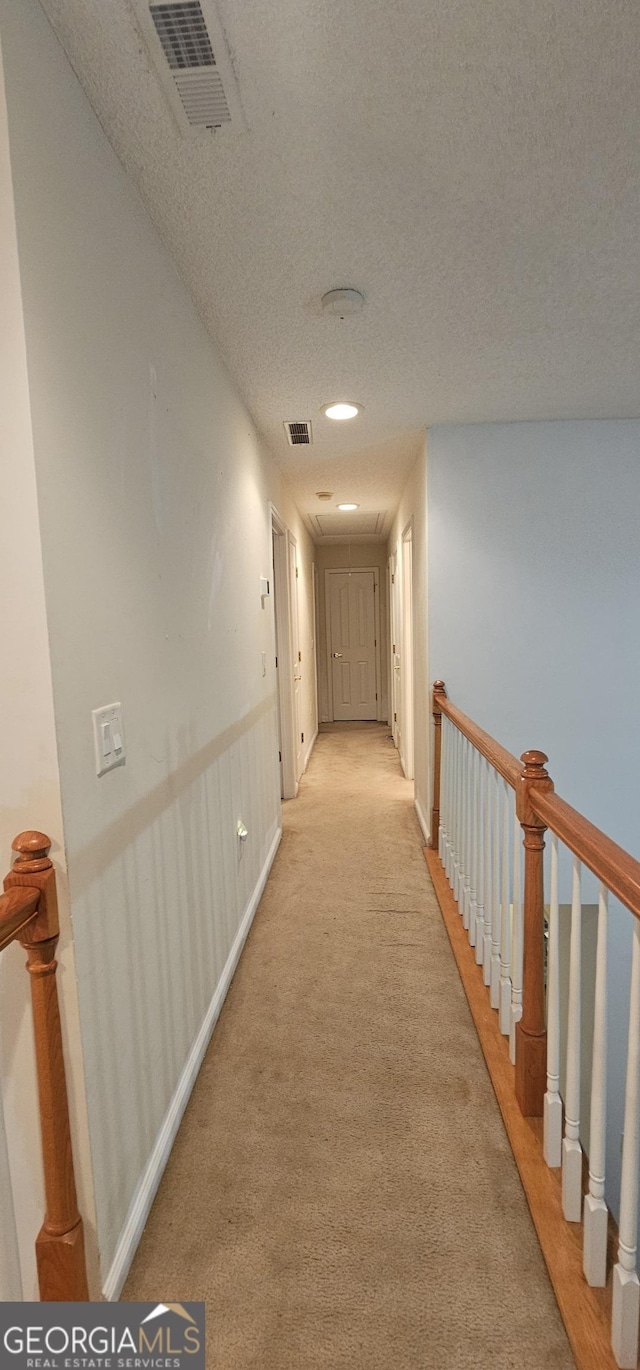 corridor featuring attic access, visible vents, light colored carpet, and a textured ceiling