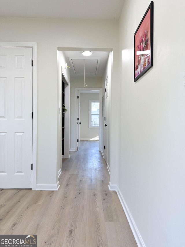 corridor with attic access, light wood-type flooring, and baseboards