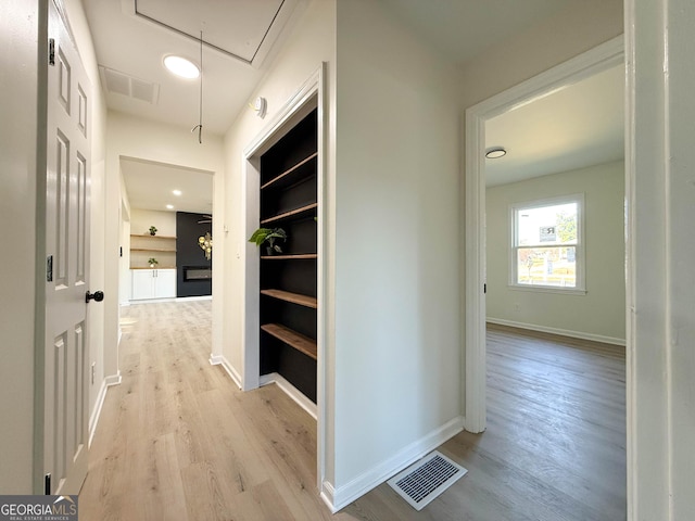 corridor with attic access, light wood-style flooring, baseboards, and visible vents