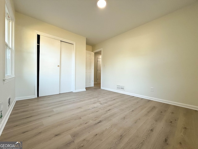 unfurnished bedroom with a closet, visible vents, light wood-type flooring, and baseboards