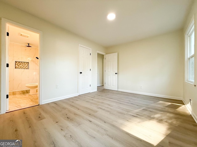 unfurnished bedroom with wood finished floors, baseboards, and connected bathroom