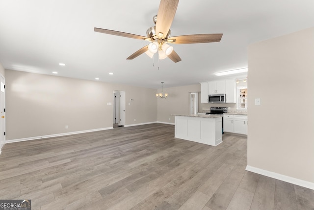 unfurnished living room with ceiling fan with notable chandelier, light wood-style flooring, baseboards, and recessed lighting
