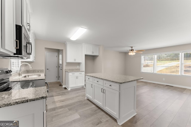 kitchen with stainless steel microwave, light wood-style floors, a ceiling fan, and white cabinets