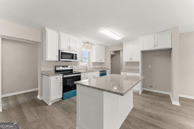 kitchen featuring range with electric stovetop, a sink, stainless steel microwave, and white cabinetry