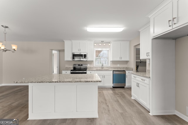 kitchen with white cabinets, light wood finished floors, a sink, an inviting chandelier, and appliances with stainless steel finishes