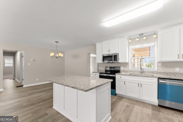 kitchen featuring light wood finished floors, stainless steel appliances, a sink, a notable chandelier, and a kitchen island