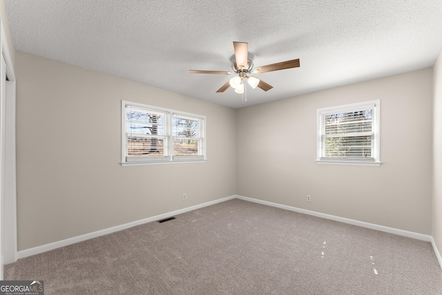 carpeted spare room featuring plenty of natural light, a ceiling fan, visible vents, and baseboards