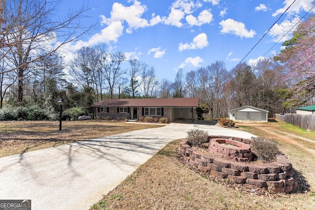 ranch-style home featuring a fire pit, stone siding, concrete driveway, fence, and an outdoor structure