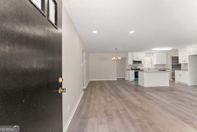 kitchen with light wood-style floors, stainless steel appliances, white cabinets, baseboards, and a notable chandelier