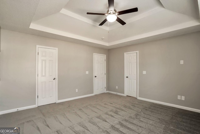 unfurnished bedroom featuring baseboards, carpet floors, ceiling fan, and a raised ceiling