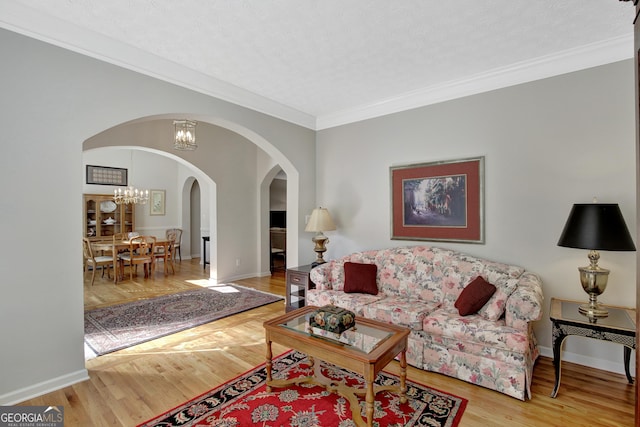 living room featuring wood finished floors, arched walkways, crown molding, baseboards, and a chandelier