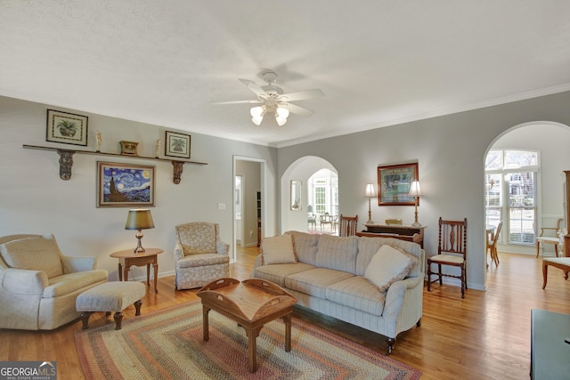 living room with arched walkways, crown molding, a ceiling fan, and light wood finished floors