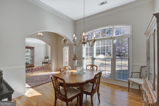 dining space with light wood-type flooring, visible vents, arched walkways, an inviting chandelier, and crown molding