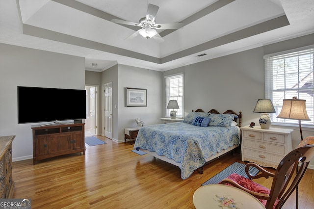 bedroom with light wood finished floors, a raised ceiling, and baseboards