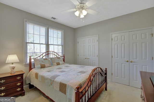 bedroom featuring visible vents, two closets, baseboards, light colored carpet, and ceiling fan