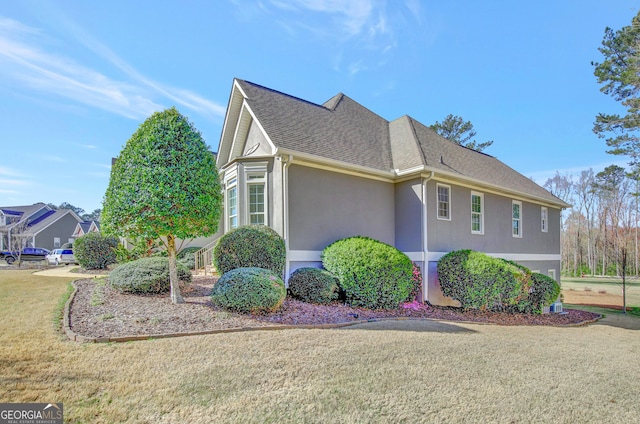 view of side of home featuring stucco siding, a yard, and a shingled roof
