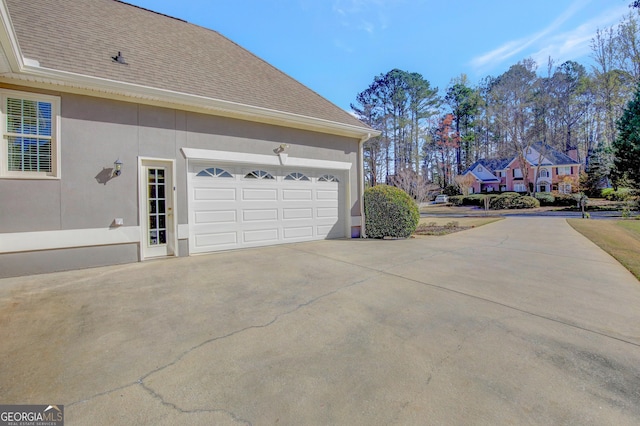 view of side of property with stucco siding, driveway, a shingled roof, and a garage