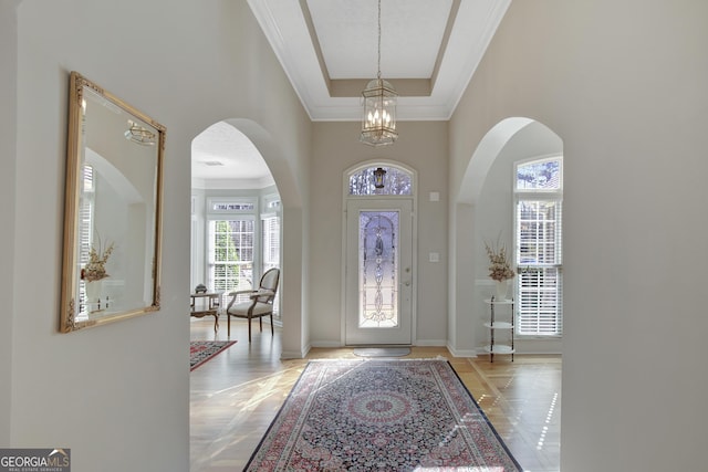 entryway featuring arched walkways, an inviting chandelier, baseboards, and ornamental molding