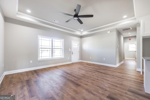unfurnished living room with ornamental molding, baseboards, ceiling fan, a tray ceiling, and dark wood finished floors