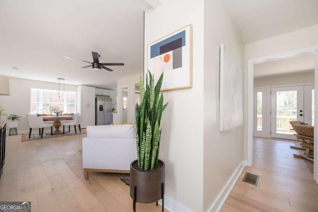 hallway with light wood finished floors, plenty of natural light, visible vents, and baseboards
