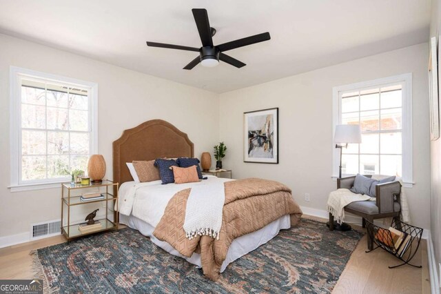 bedroom with a ceiling fan, wood finished floors, visible vents, and baseboards