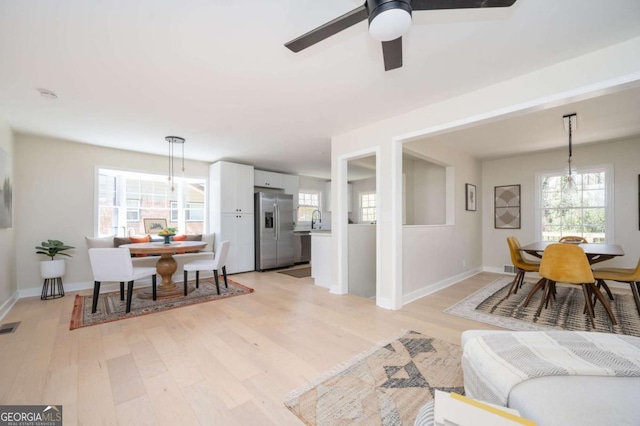 living area featuring visible vents, baseboards, a ceiling fan, and light wood finished floors