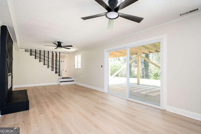 unfurnished living room with a ceiling fan, visible vents, light wood-style flooring, stairs, and a textured ceiling