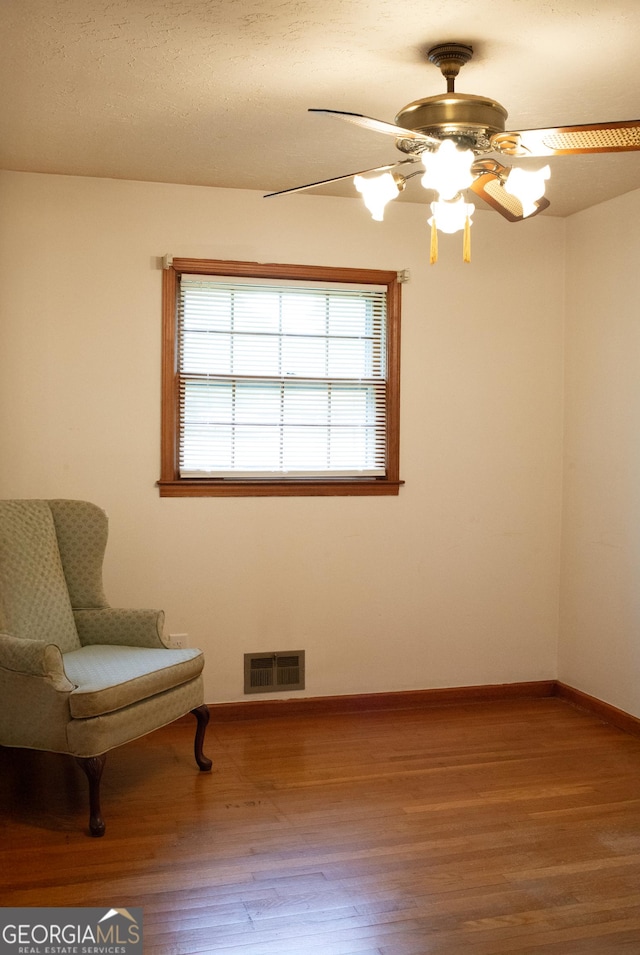 living area featuring baseboards, a ceiling fan, wood finished floors, and visible vents