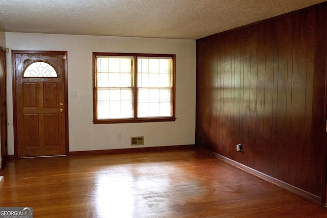 entrance foyer with wooden walls, visible vents, wood finished floors, and a wealth of natural light