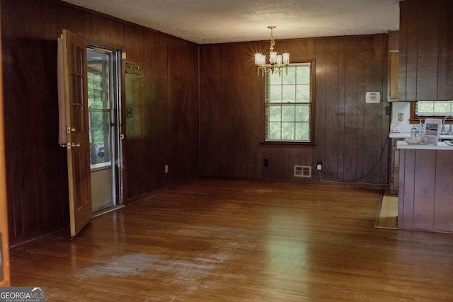 unfurnished dining area with a textured ceiling, visible vents, wood finished floors, a chandelier, and wooden walls
