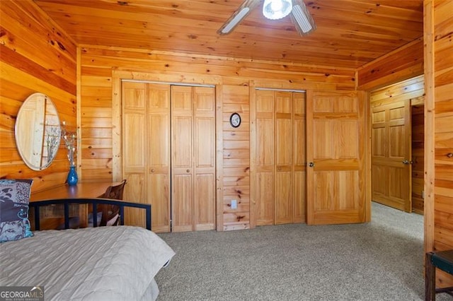 bedroom with carpet flooring, wooden walls, multiple closets, and wood ceiling
